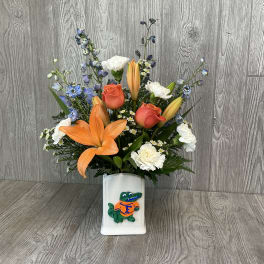 Orange lilies and roses in a white vase with a Florida Gators logo