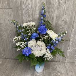 Tall blue and white flower arrangement with carnations, mums, hydrangea and a crown accent in a blue vase.
