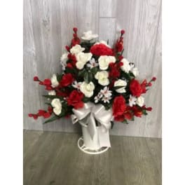 Red and white floral arrangement in a white vase with a satin bow