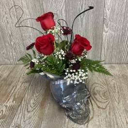 Red roses and small white flowers arranged in a glass skull vase