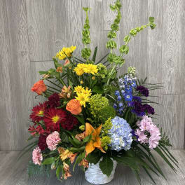 Tall mixed-color flower arrangement with lilies, roses, mums, and hydrangea in a white basket.