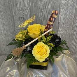 Yellow roses in a black vase with a decorative wand and wing ornament