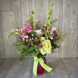 Mixed pink and green floral arrangement in a magenta vase with a lime ribbon