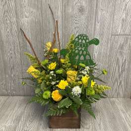 Yellow floral arrangement in a wooden box with a green turtle decoration