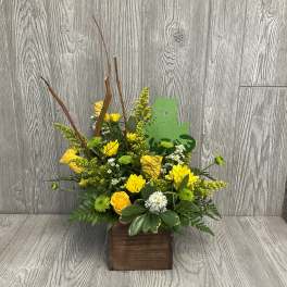 Yellow and white flowers arranged in a wooden box with a green frog decoration