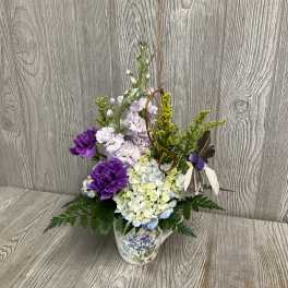 Purple and pale hydrangea arrangement in a floral mug with decorative accents