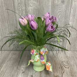Purple tulips arranged in a green vase with a floral ribbon