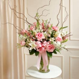 Pink roses and white lilies arranged in a glass vase with a pink ribbon