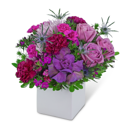 Purple and pink floral arrangement in a white square vase