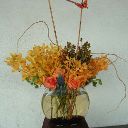 Orange and yellow floral arrangement in a round glass vase