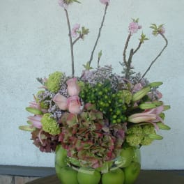 Pink flowers and green apples arranged in a glass bowl