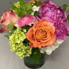 Compact arrangement of orange roses, pink blooms, and green hydrangea in a clear glass vase