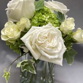 Small white rose and green hydrangea arrangement in a clear glass vase