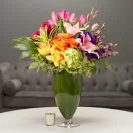 Colorful bouquet of mixed flowers in a tall green glass vase