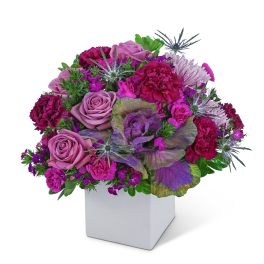 Purple and pink floral arrangement in a white square vase