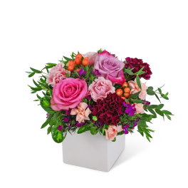 Pink and purple rose arrangement in a white square vase