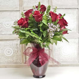 Red roses arranged in a glass vase with a burgundy ribbon