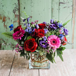 Mixed bouquet of red roses, pink gerberas, and purple flowers in a glass vase