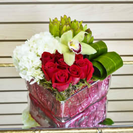 Red roses and white hydrangea in a pink gift box with green orchid petals