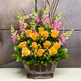 Yellow roses and pink snapdragons in a brown ceramic vase