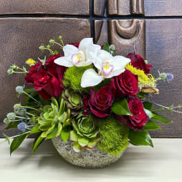 Red roses and white orchids in a stone bowl with succulents