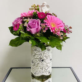 Pink and lavender flowers arranged in a lace-wrapped glass vase