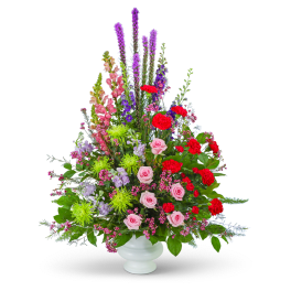Tall mixed floral arrangement in a white urn vase with pink and red blooms