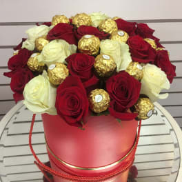 Red and white roses arranged with gold-wrapped chocolates in a pink hat box