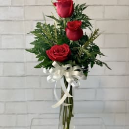 Three red roses in a clear glass vase with a white ribbon