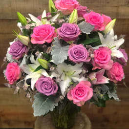 Bouquet of pink and lavender roses with white lilies in a glass vase