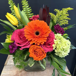 Bright mixed bouquet with orange gerbera, pink roses, and yellow tulips in a glass vase