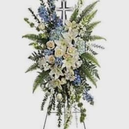 Standing funeral spray with white lilies, blue flowers, and a cross