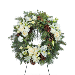White floral wreath with roses, lilies, and pinecones on a stand