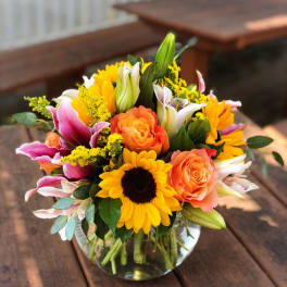 Bouquet of sunflowers, orange roses, and pink lilies in a glass vase
