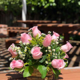 Pink roses arranged in a woven basket with small white filler flowers