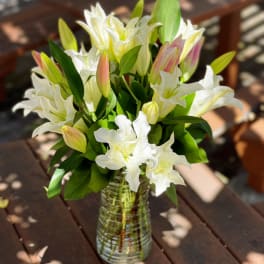 White lilies in a clear glass vase on a wooden table