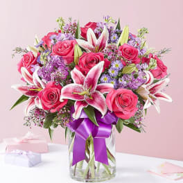 Pink roses and lilies in a glass vase with a purple ribbon