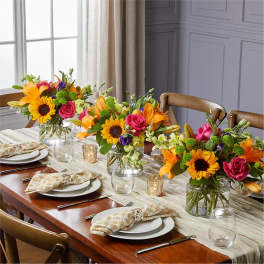 Three colorful floral centerpieces in glass vases on a set dining table