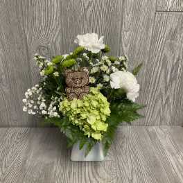 White and green floral arrangement with a teddy bear pick in a silver vase
