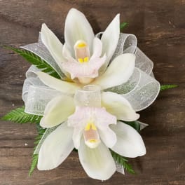 White orchid corsage with silver ribbon on a wooden surface