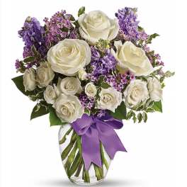 Medium glass vase of white roses and purple flowers with a purple ribbon bow