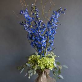 Tall blue flower arrangement with green hydrangeas in burlap wrap