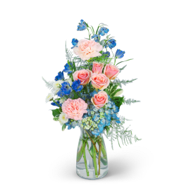 Pink roses and blue flowers arranged in a clear glass vase