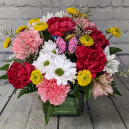 Mixed bouquet of carnations and daisies in a green vase with a butterfly pick