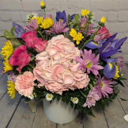 Mixed bouquet of pink, purple, yellow, and white flowers in a white vase