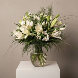 White lilies arranged in a clear glass vase with airy greenery