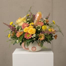 Mixed bouquet in a white mug-style vase with yellow and pink flowers