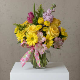 Mixed bouquet of yellow and pink flowers in a glass vase with a patterned ribbon