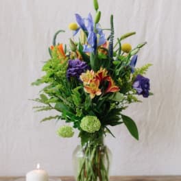 Tall mixed bouquet in a clear glass vase beside a lit candle