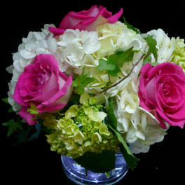 Compact arrangement of hot pink roses and white hydrangeas in a clear glass vase